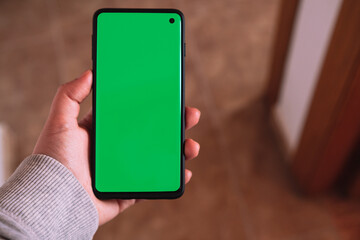 Woman hand showing smartphone green screen. Chroma key phone screen in vertical position. Photo mockup with copy space. Internet of things. New technology concept.