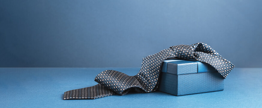 Happy Fathers Day background banner. Two blue gift boxes with ribbon bow and necktie on dark blue table. Monochrome. Gift delivery for him. Male fashion