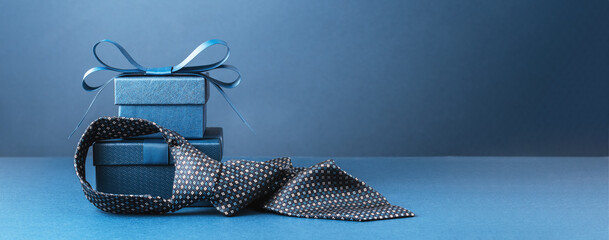Happy Fathers Day background banner. Two blue gift boxes with ribbon bow and necktie on dark blue table. Monochrome. Gift delivery for him. Male fashion - obrazy, fototapety, plakaty