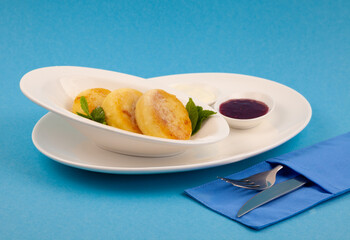 Round cottage cheese pancakes in a white plate on a blue background. Food breakfast. Healthy food. Sour cream sauce and mint. Top view closeup. Dessert meal. Curd cheese pancake ricotta fritters.