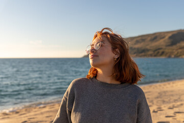 redhead woman with glasses smiling on a beach