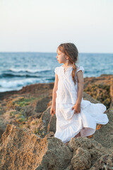 Fototapeta na wymiar Child girl in white clothes standing on rocks on the background of the blue sea