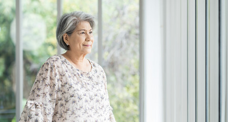 Senior Asian woman standing alone near windows in hospital. Old Asian female using walking stick at home. Retirement, health care and ageing concept