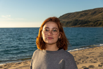 redhead woman with glasses smiling on a beach