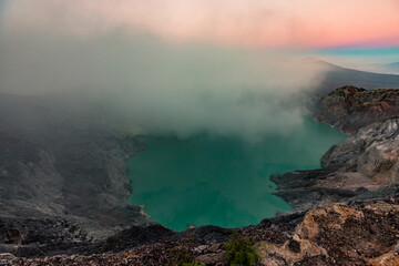 Fototapeta na wymiar Sunrise over Kawah Ijen Volcano revealing acid turquoise lake and toxic sulfur gases and dead trees next to illegal mining operation, Java, Indonesia