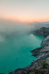 Sunrise over Kawah Ijen Volcano revealing acid turquoise lake and toxic sulfur gases and dead trees next to illegal mining operation, Java, Indonesia