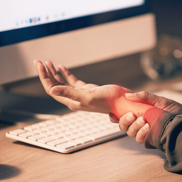 Woman, hands and wrist pain by computer from carpal tunnel syndrome or overworking at night by office desk. Hand of female holding painful arm area or pressure by PC from working late at workplace