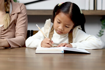 Asian little cute girl learning and studying her lesson with mother at home, schoolgirl pupil doing homework with tutor teacher, happy child student writing in notebook, homeschool kid education.