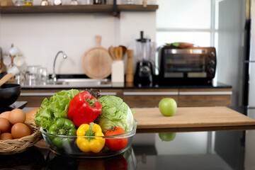 Colorful fresh vegetables salad in a glass cup and food ingredients on table counter kitchen with blurred background of beautiful modern kitchen, healthy natural food concept with copy space.