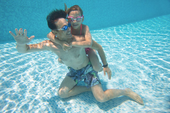 underwater photo of young dad with little girl in swimming  pool