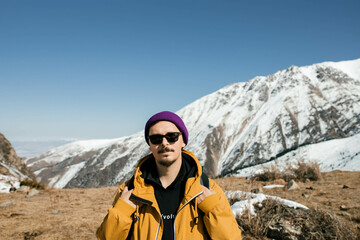 A man stands with his back to the mountains, looking at the camera