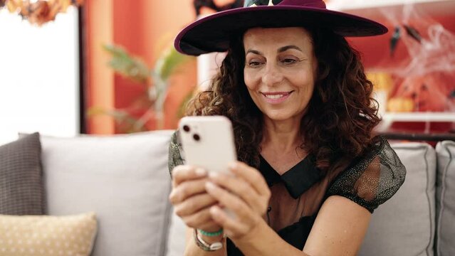 Middle age hispanic woman using smartphone having halloween party at home
