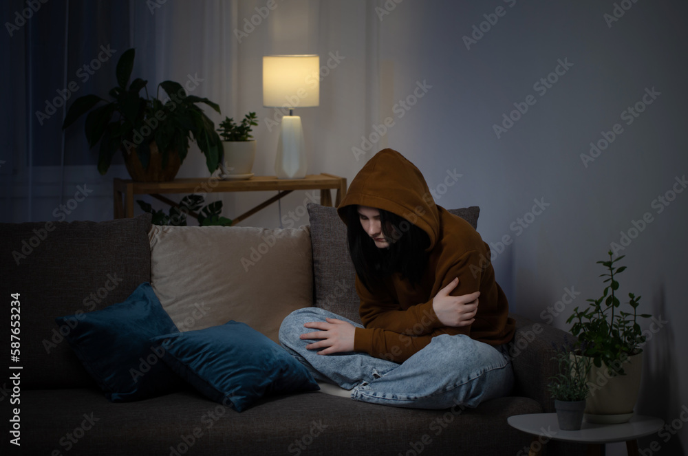 Wall mural sad teenager girl sitting on couch indoor at night