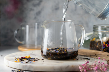 Adding hot water to glass tea pot with loose black leaf tea. Making tea.