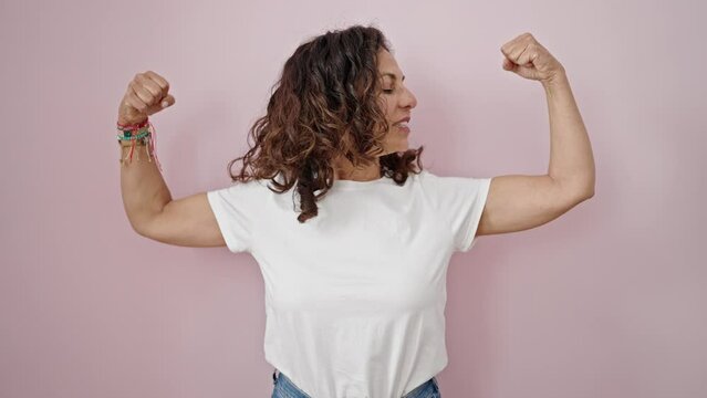 Middle age hispanic woman smiling confident doing strong gesture with arms over isolated pink background