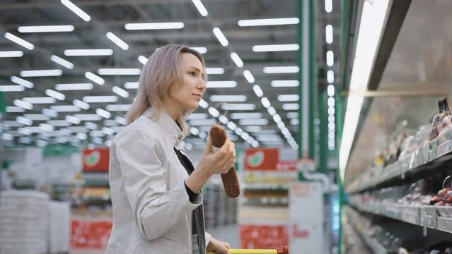 The buyer in the supermarket chooses the sausage next to the shelves. Woman at the Grocery Store