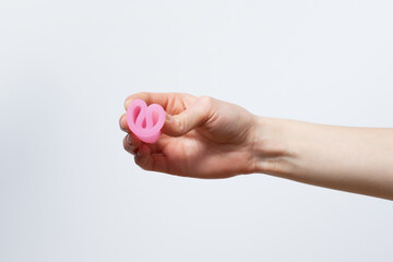 Female hand holding a pink menstrual cup and showing how to fold it on a white isolated background. Instructions for use. Image for your design