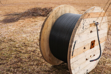 Wooden coil of electric cable, in its natural form. Electric black cable on wooden coils outdoors. Selective focus.