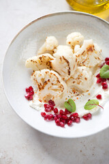 Plate with roasted cauliflower florets, cream-cheese and pomegranate seeds, vertical shot on a light-beige stone background, middle close-up