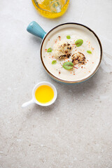 Cauliflower cream-soup in a turquoise serving bowl, vertical shot on a beige stone background, high angle view, copy space