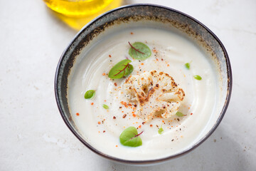 Bowl of cauliflower cream-soup topped with roasted cauliflower floret, horizontal shot on a light-beige stone background, middle closeup