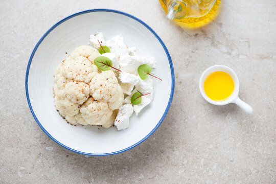 White plate with steamed cauliflower cabbage and feta cheese, flat lay on a beige stone background, horizontal shot