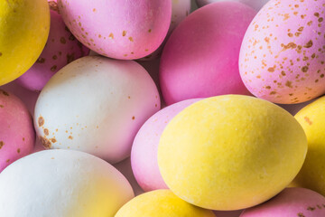Colored sweet little eggs. Multi-colored Easter eggs on a plate. Sweet Easter eggs shot close up. Festive chocolate eggs in pink, white and yellow
