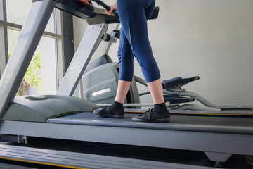 Women's legs in tight pants and black sneakers on a treadmill in the gym. The concept of a healthy lifestyle, weight loss.