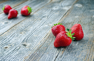 Reife rote Erdbeeren aus biologischem Anbau angeboten als close-up auf einem grauen ausgebleichten Holz Board mit Textfreiraum links 