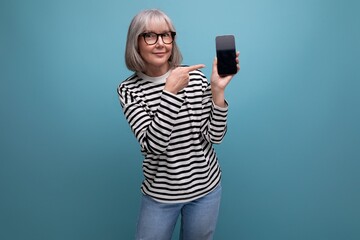 portrait of a fashionable 60s old lady holding a smartphone with a mockup on a bright background with copy space