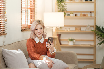 Young asian woman using a smart phone sitting on the sofa in the room. Order some online shopping.