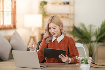 Portrait of Asian young woman working using smartphone computer or tablet working online at home office , freelance business online concept.