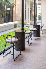 Chairs and tables and the glass wall in the cafe.  Interior of cafe with empty table and chairs, tall transparent glass wall as background. also can see the green garden outside the room through the g