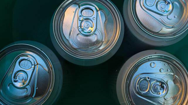 Beer in aluminum cans is cooled in a green bucket with cold water