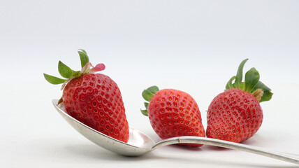 close up of a strawberry in a spoon with some strawberries around it on a white background
