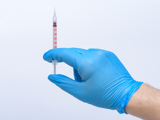 Strzykawka z igłą trzymana przez lekarza w niebieskich nitrylowych rękawiczkach 
