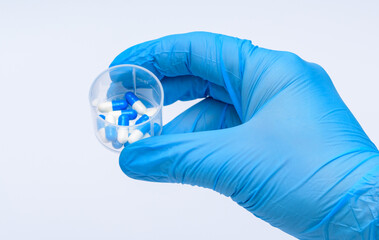 Fiolka z lekarstwami trzymana w dłoniach w niebieskich rękawiczkach medycznych na białym tle