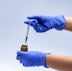 Dłonie w niebieskim rękawiczkach medycznych ze strzykawka z igłą  i pojemnikiem - pobieranie próbki do badań - obrazy, fototapety, plakaty