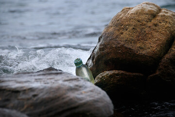 A discarded plastic bottle stuck between boulders at the beach showing awareness of ocean plastic pollution and earth day