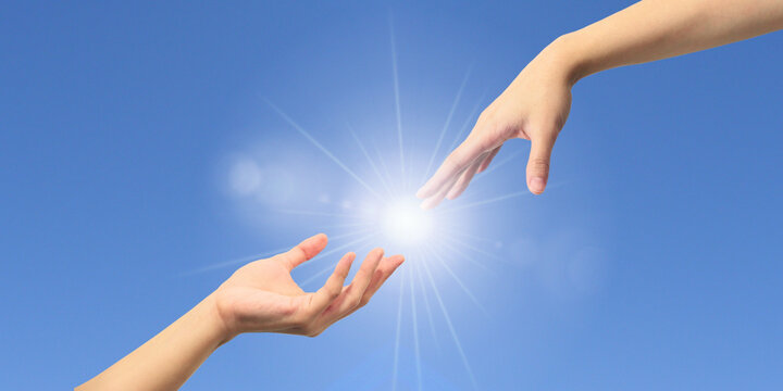 Helping hands emerging from a blue sky. God reaching out to praying hands on a beautiful sky background to save and support people. Religious or business concept.