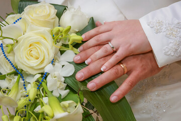 Obraz na płótnie Canvas Groom and the bride with white wedding bouquet outdoors close-up. Hands with wedding rings. Close-up on the hands of a Caucasian couple holding the bridegroom roses bouquet.