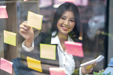 smiling pretty businesswoman write down on colorful sticker paper, happy young female writing memos idea plan on paper notes