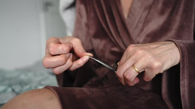 mature woman hands close-up using nail scissors for manicure at home