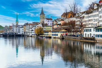 Naklejka na ściany i meble Cityscape or beautiful landscape of Zurich's old town in winter blue sky.People walk along Limmat river.Clock tower with cloud.Vintage city in Europe.River with reflection.Panorama style.