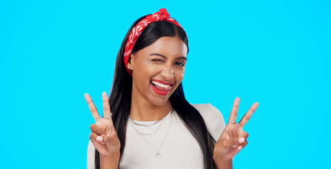 Face, funny and Indian woman with peace sign, confident and happiness on a blue studio background....