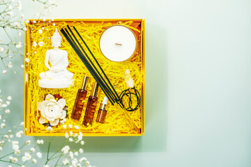 Holiday composition with recovering kit for meditation, yoga and relaxation. Yellow gift box with buddha statue, aroma sticks, natural oils, candle and crystals. Preparing healthy surprise. Copy space