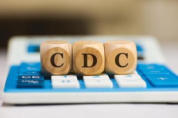 A sigla CDC para Código de Defesa do Consumidor em Português do Brasil escrita em dados de madeira que estão sobre uma calculadora azul. - obrazy, fototapety, plakaty