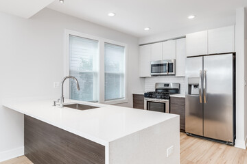 A modern kitchen with stainless steel appliances, a waterfall granite island, a light hardwood...