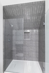 A walk-in shower with dark grey subway tiles, a built-in shelf, glass door, and chrome showerhead.