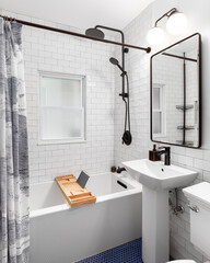 A bathroom with a white subway tile shower and black faucet, blue circular tile floor, and a white...